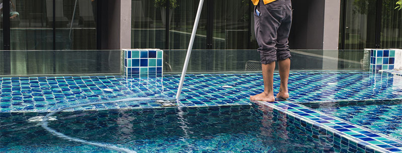 Hose filling a blue-tiled swimming pool while a person stands on the pool ledge